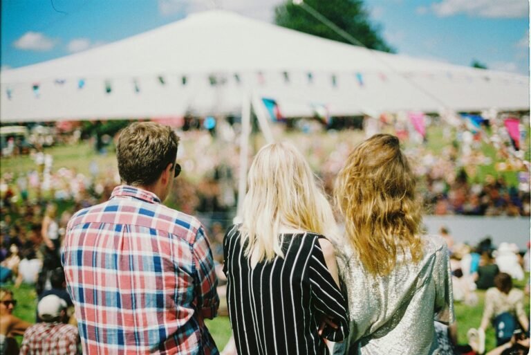 Three friends enjoying a sunny day at an outdoor summer festival, viewed from behind.