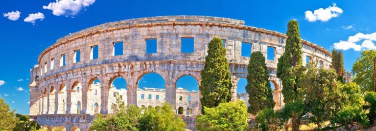 Ancient Roman amphitheater in Pula, Istria, with its massive stone arches and surrounding trees on a sunny day.