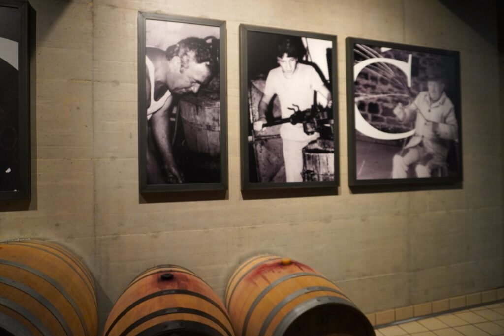 Historical black-and-white photos of winemakers at work, displayed in a modern winery with oak barrels.