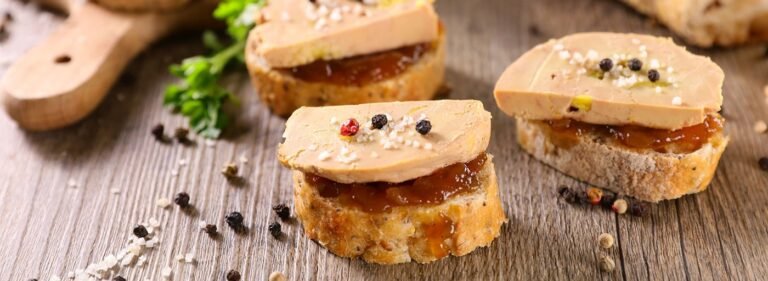 Slices of foie gras on toasted baguette with jam and pepper garnish.