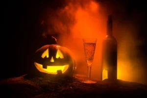 Glowing jack-o'-lantern next to a glass of wine and a wine bottle, set against an eerie orange backdrop.