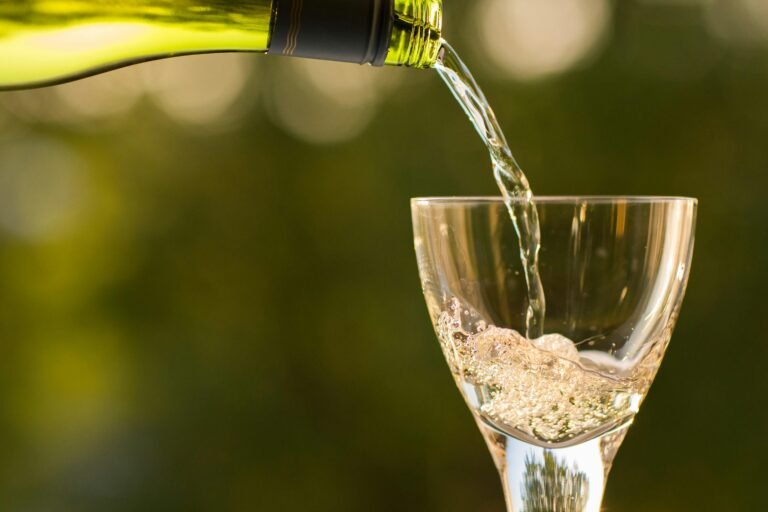 White wine being poured into a glass with a green garden backdrop