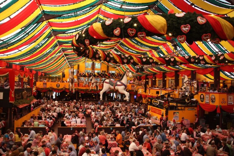 Festive Oktoberfest tent filled with people, decorated with colorful banners and hanging ornaments.