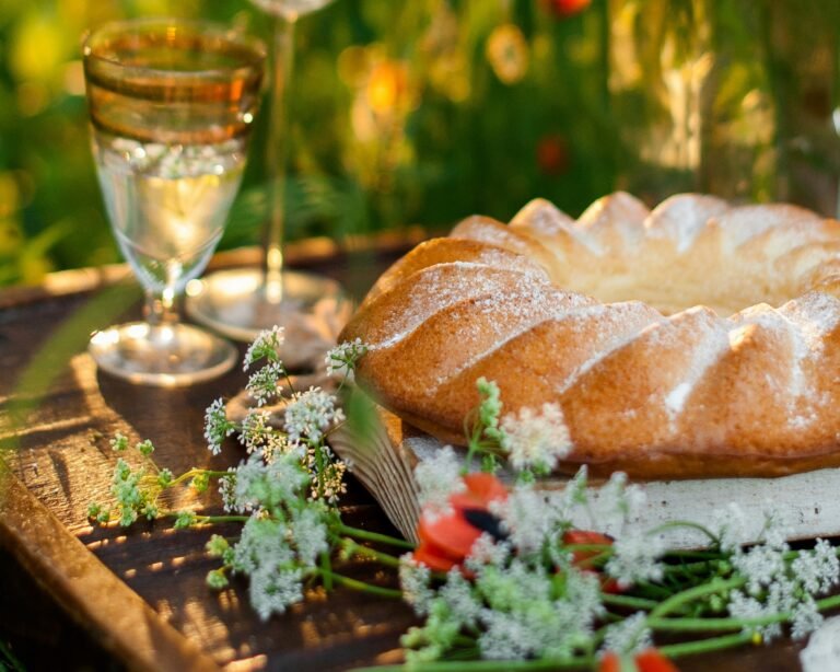 A rustic outdoor setting with a cake and a glass of white wine surrounded by flowers, capturing a cozy atmosphere.