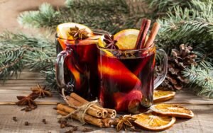 Warm mulled wine served in glass mugs with cinnamon sticks, orange slices, and star anise, surrounded by festive decor and dried oranges.
