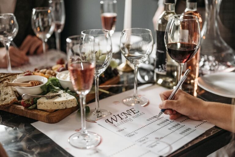 A wine tasting setup featuring various glasses of wine, a tasting notes sheet, cheese, and a selection of fruits and bread on a wooden platter.