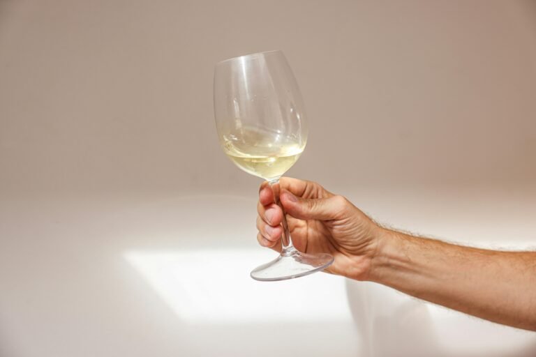 A close-up of a hand holding a glass of white wine against a softly lit background, emphasizing elegance and simplicity.