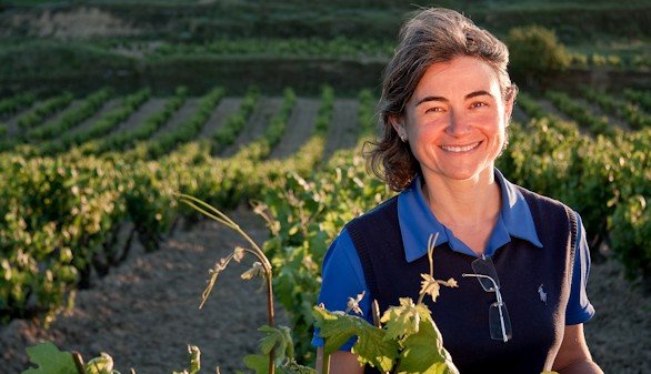 Smiling woman in a vineyard during golden hour, showcasing her connection to winemaking.