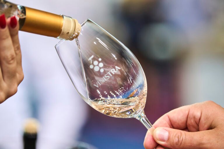 Close-up of white wine being poured into a Vinistra branded wine glass, showcasing elegance and wine craftsmanship.