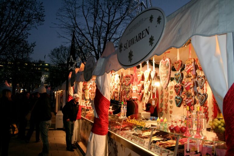 Christmas market stall selling traditional gingerbread hearts, sweets, and festive treats, illuminated at night with holiday decorations.