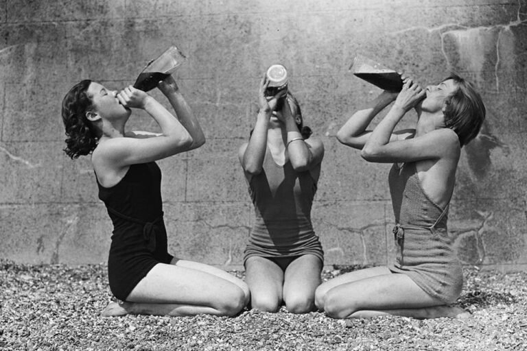 Vintage photo of three women in swimsuits enjoying wine outdoors, representing carefree summer vibes.