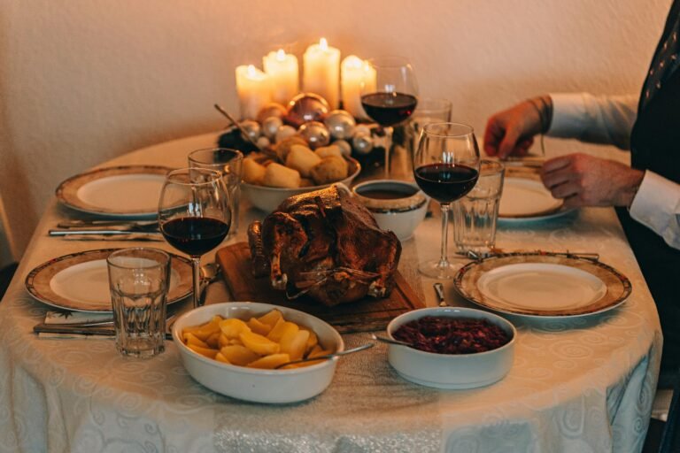 A cozy holiday dinner table with candles, roasted turkey, and wine glasses, set for a festive meal.