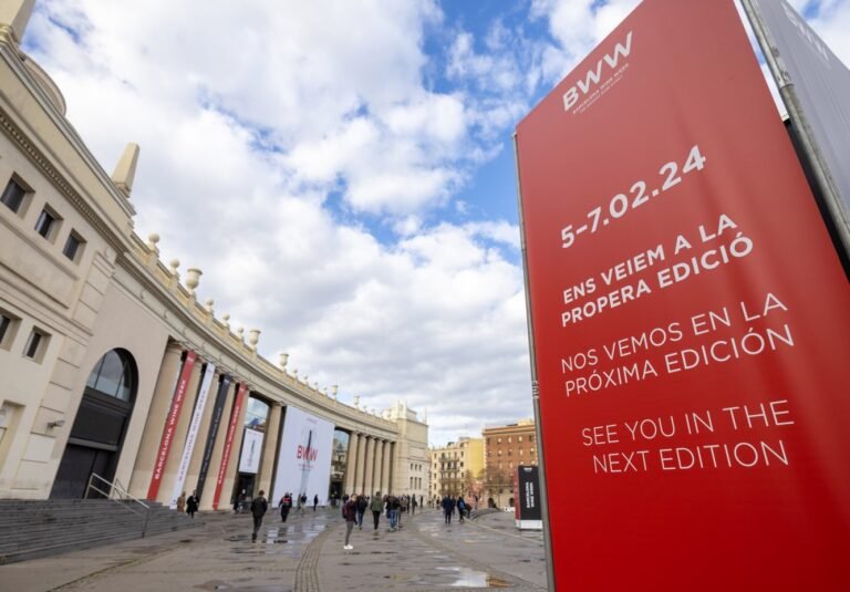 Entrance to the Barcelona Wine Week 2024 event, with a red sign announcing the next edition and a historic building in the background, welcoming wine professionals and enthusiasts.