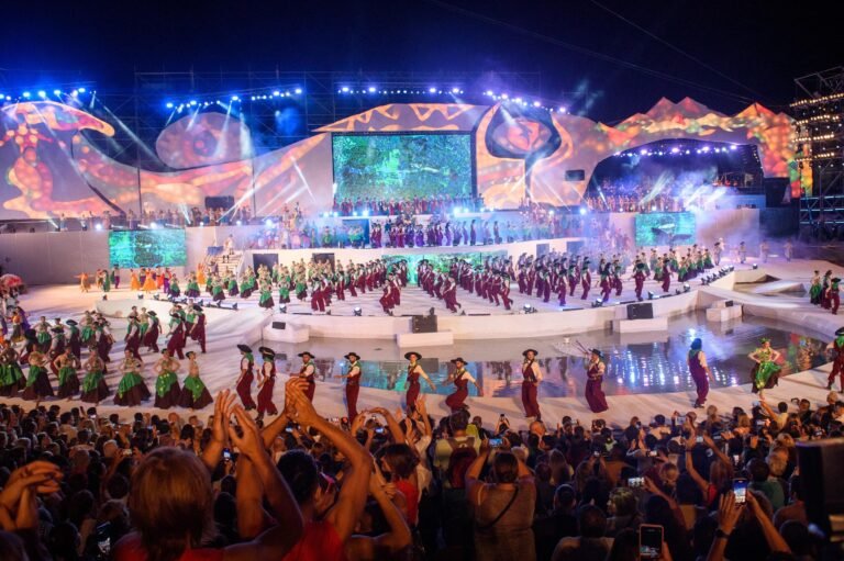 Vibrant outdoor festival with dancers in colourful costumes performing on a grand stage with dazzling lights and an enthusiastic crowd.