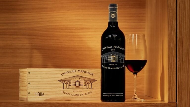 Château Margaux 2015 Premier Grand Cru Classé bottle with a wooden case and a glass of red wine, elegantly displayed on a wooden shelf.