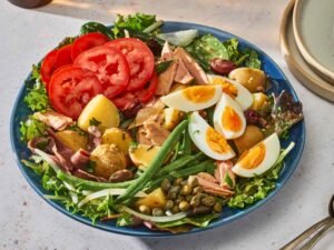 Classic Niçoise salad with new potatoes, hard-boiled eggs, tuna, anchovies, tomatoes, green beans and olives on a bed of mixed greens.