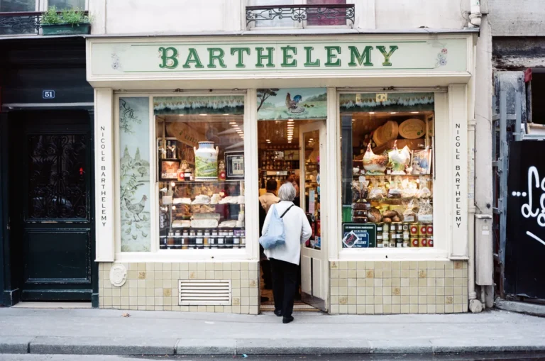 The charming exterior of Barthélemy, a traditional French cheese shop in Paris, with a customer stepping inside to explore fine artisanal cheeses.