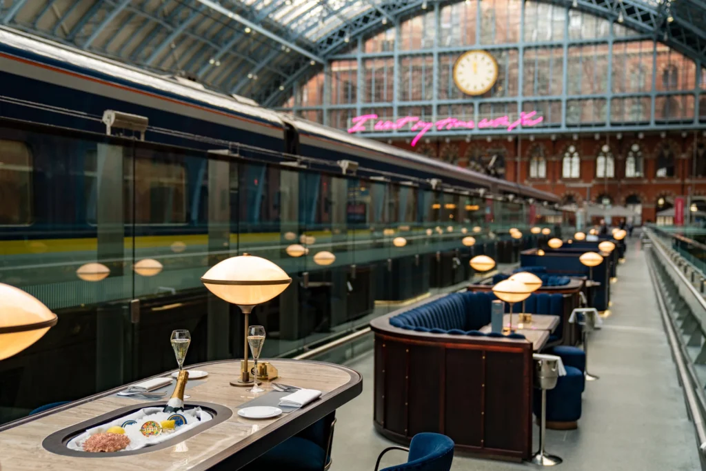 Elegant champagne dining setup at a train station restaurant with the Eurostar train in the background at London St Pancras International.