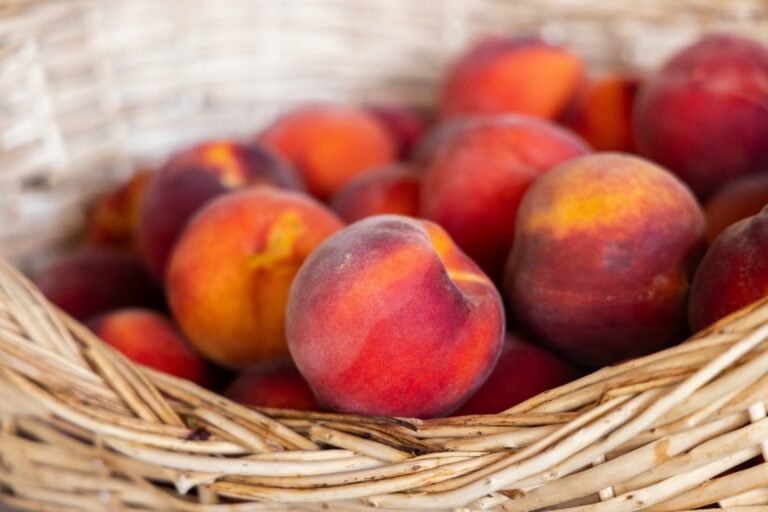 Ripe peaches with a velvety skin in warm tones of red and orange, arranged in a rustic wicker basket.