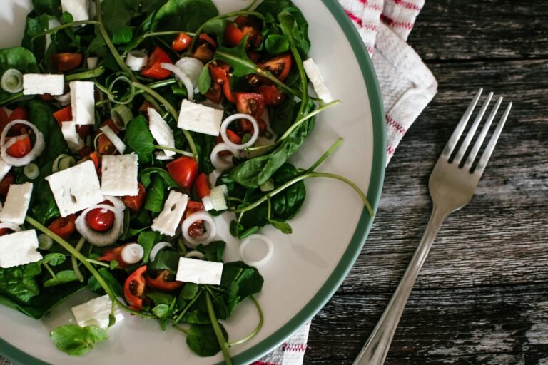 Fresh spinach salad with cherry tomatoes, feta cheese cubes, and sliced spring onions served in a white dish.