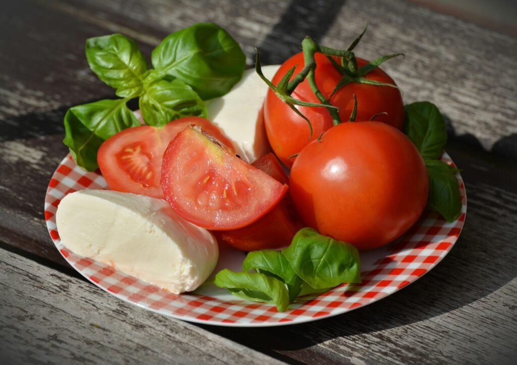 Italian Caprese salad with ripe tomatoes, mozzarella cheese, and fresh basil leaves on a red-checked plate.