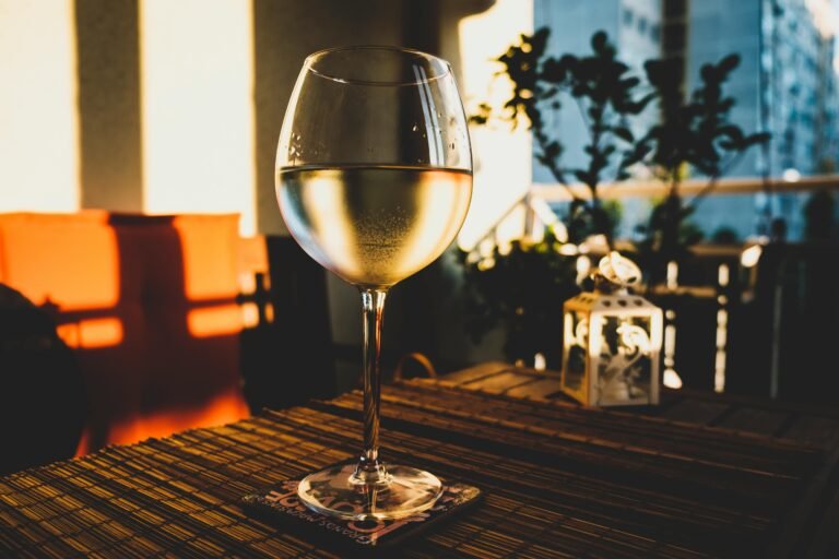 Chilled glass of white wine on a balcony table at sunset, with warm golden lighting and an urban view in the background.
