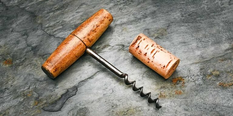 Vintage wooden-handled corkscrew with a removed wine cork on a textured stone surface.