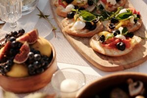 Rustic Italian bruschetta with olives, basil, tomatoes, and mozzarella served on toasted bread, alongside a bowl of fresh figs and grapes