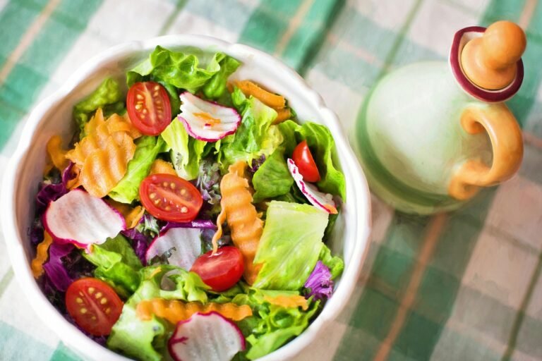 Colourful fresh green salad with lettuce, cherry tomatoes, radishes, carrots, and a ceramic dressing jar on a green checked tablecloth