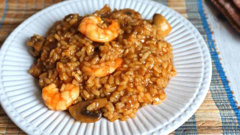 Creamy Spanish arroz meloso with prawns and mushrooms served on a white plate.