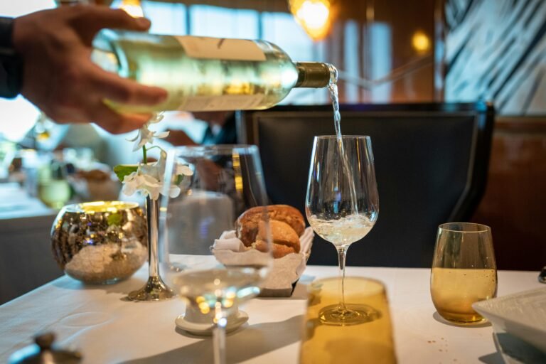 White wine being poured into a glass at a fine dining restaurant table with bread and elegant decor.