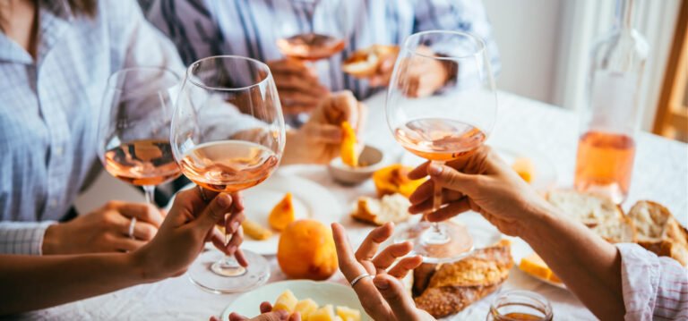 Friends toasting with glasses of orange wine during a meal with bread, cheese, and fruit.