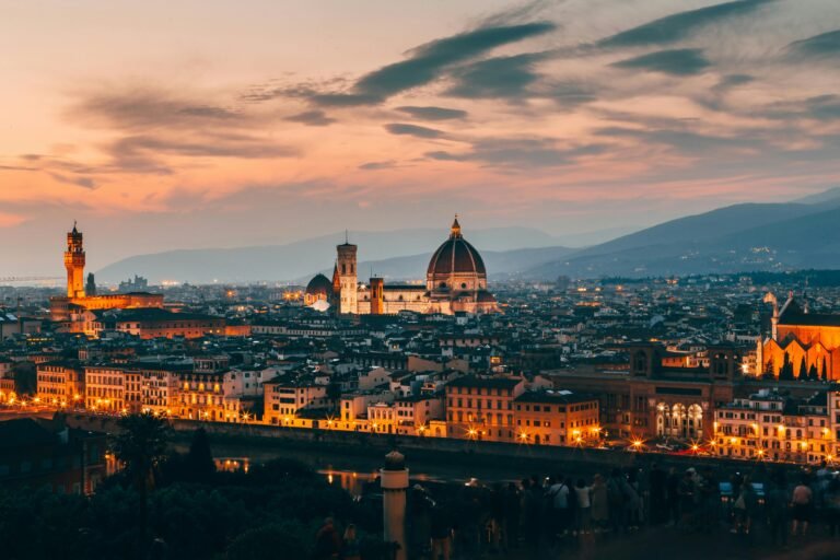 Sunset view of Florence with the Cathedral of Santa Maria del Fiore and Palazzo Vecchio illuminated over the city skyline.