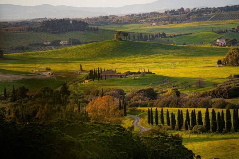 Picturesque Tuscan countryside with rolling green hills, cypress trees, and a rustic farmhouse bathed in golden evening light.